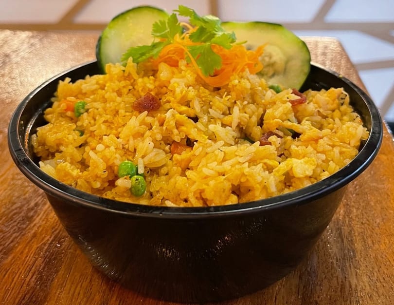 Golden fried rice with peas, carrots, and egg, garnished with cucumber and cilantro.