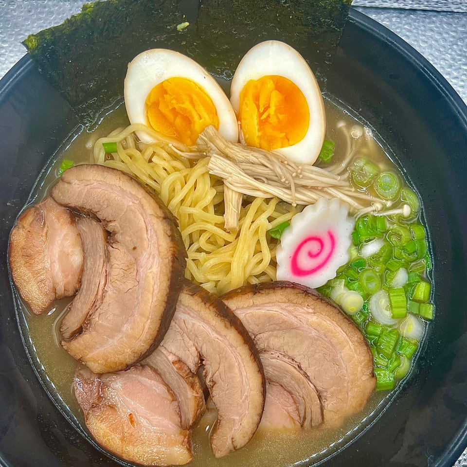 A bowl of ramen with pork slices, soft-boiled eggs, noodles, green onions, and nori.