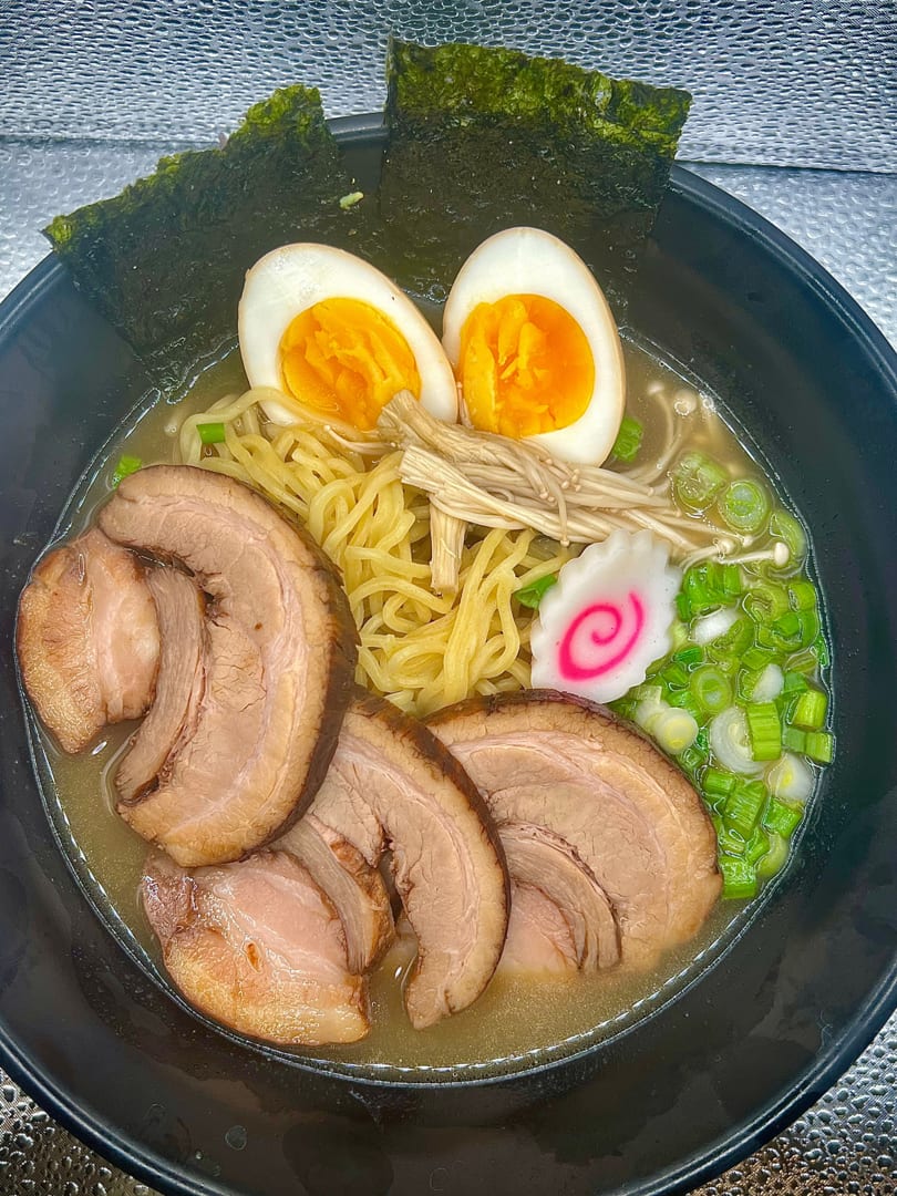 A bowl of ramen with pork slices, soft-boiled eggs, noodles, green onions, and nori.