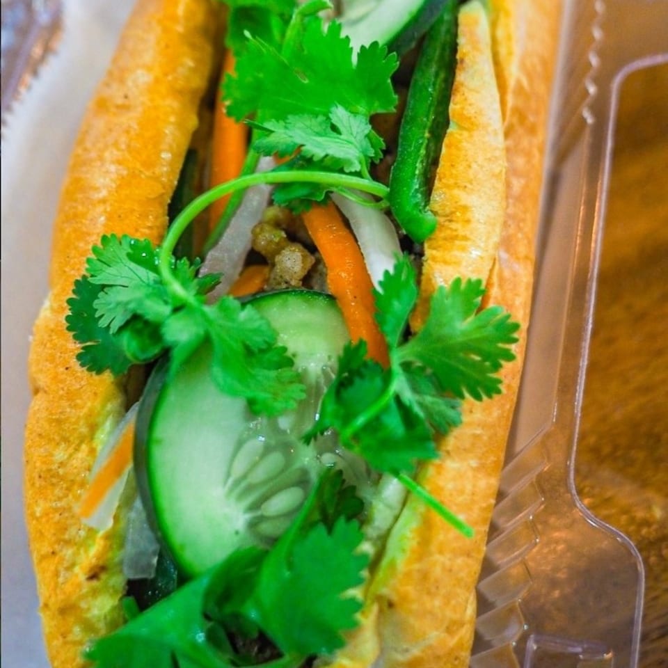 A vibrant banh mi sandwich filled with fresh cilantro, cucumber, carrots, and meat in a baguette.