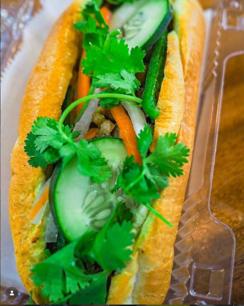 A vibrant banh mi sandwich filled with fresh cilantro, cucumber, carrots, and meat in a baguette.